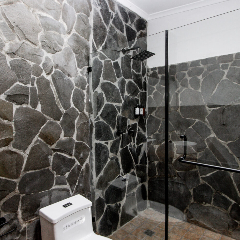 Imagen del baño de la Suite en Los Abetos Boutique Hotel, con paredes de piedra natural y una moderna ducha de vidrio, ofreciendo una experiencia exclusiva y rústica.